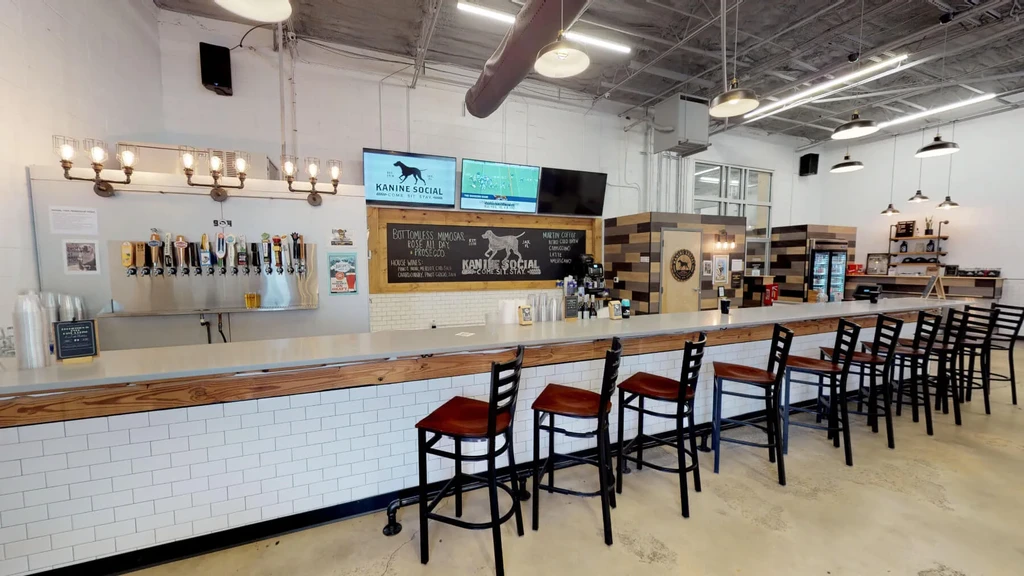 Modern industrial bar with long counter, beer taps, and Kanine Social menu.