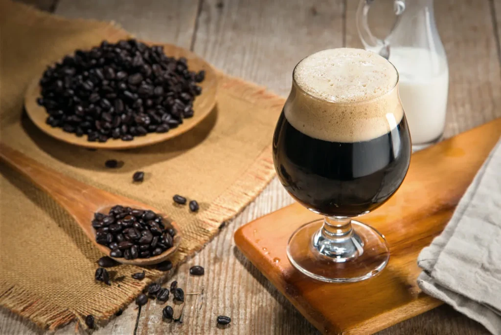 Dark foamy beverage in glass with roasted coffee beans and milk.
