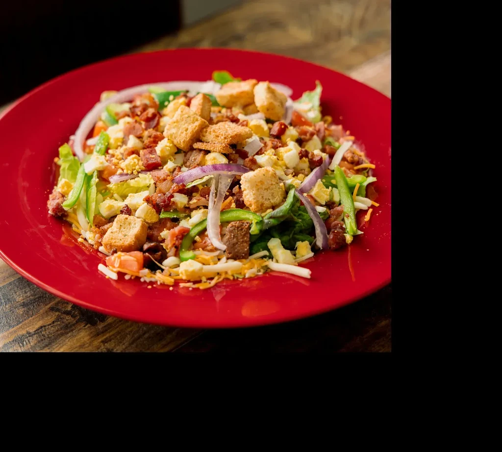 Mixed salad with lettuce, bacon, egg, cheese, croutons, on red plate.