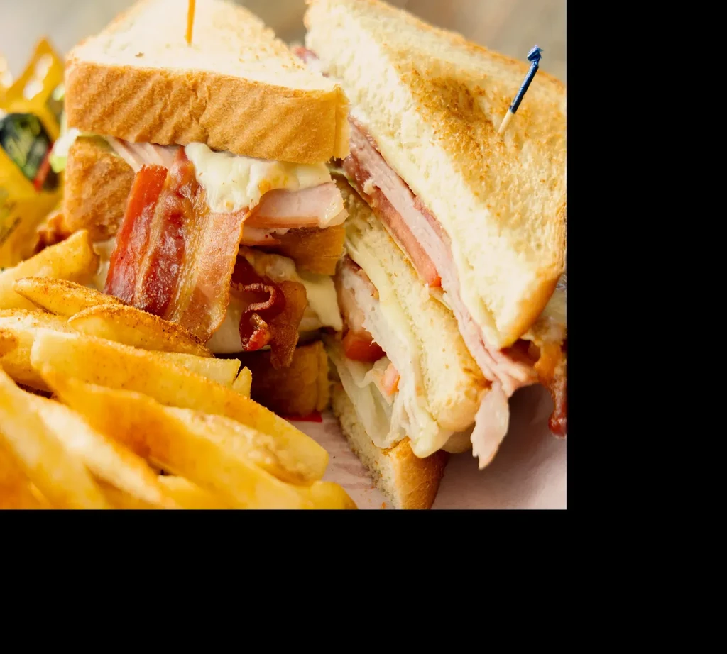 Toasted club sandwich, cut in half, with a side of french fries.