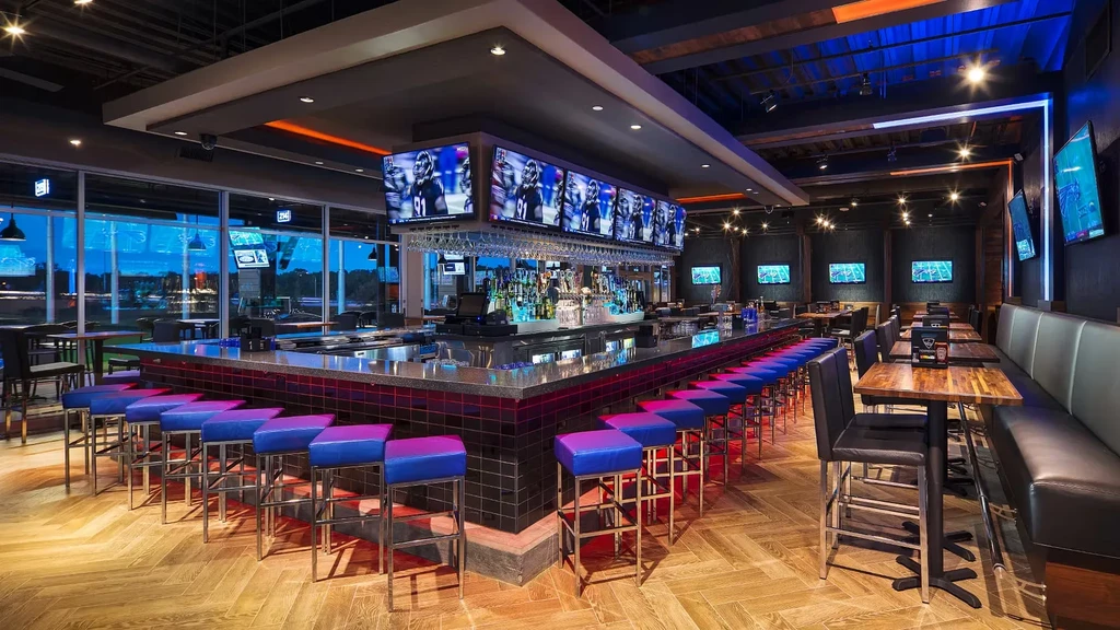 Modern sports bar interior with illuminated bar, many TVs showing sports.