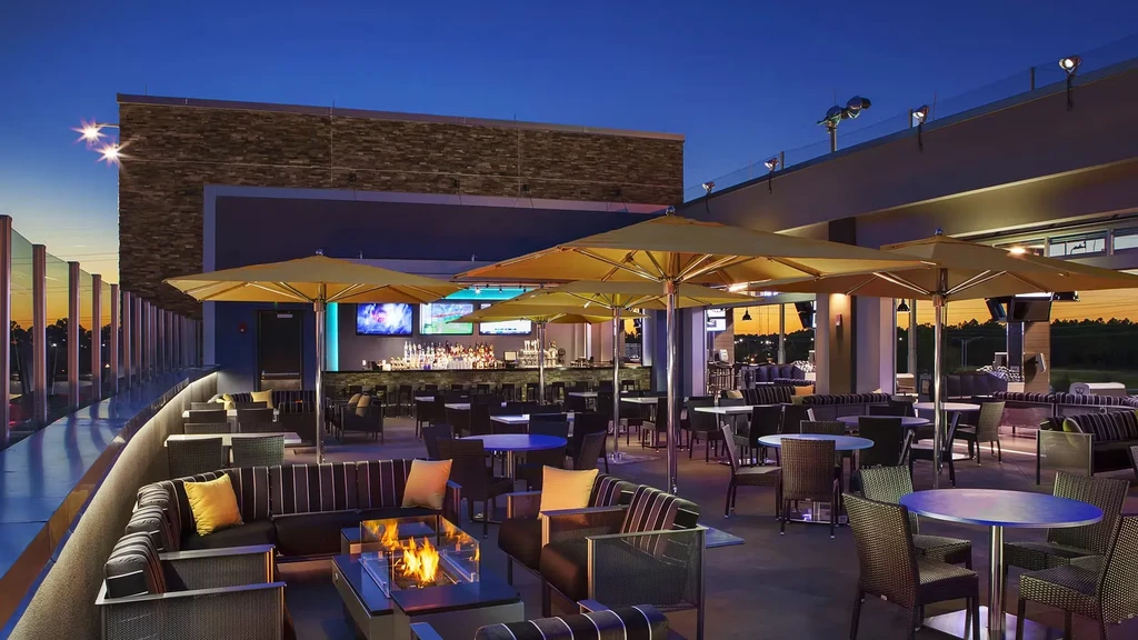 Modern rooftop bar lounge with fire pit, screens, and umbrellas.