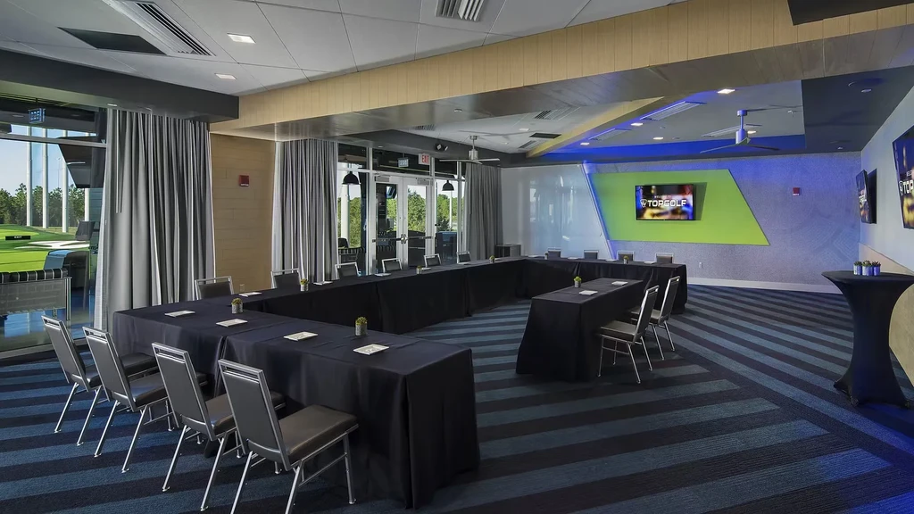 Empty Topgolf meeting room with U-shaped tables overlooking golf bays.