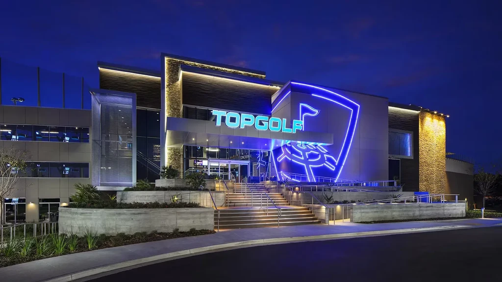 Modern Topgolf building with illuminated blue neon signs and golf bays.