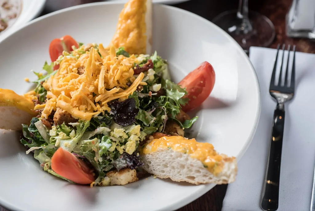 Fresh salad with lettuce, cheddar cheese, bacon, tomatoes, and dressing.