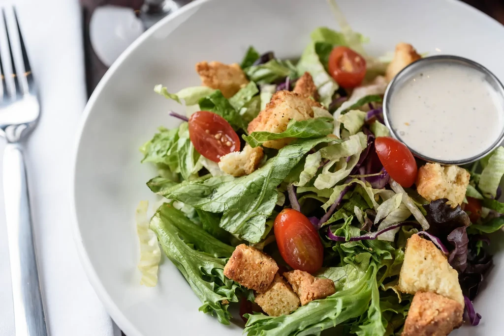 Fresh salad with lettuce, croutons, tomatoes, dressing, and a fork.