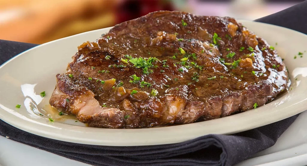 Charred steak with dark sauce, caramelized onions, and herbs on white plate.