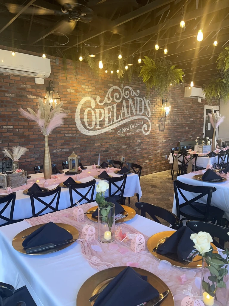 Copeland's restaurant interior, brick walls, set tables with pink decor, string lights.