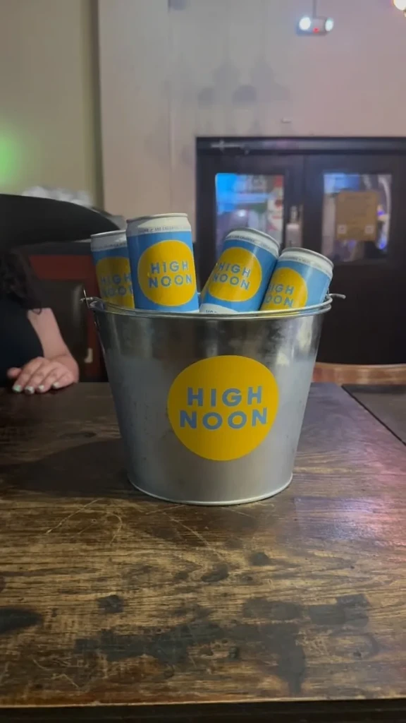 Galvanized bucket with High Noon seltzers on a rustic wooden table.