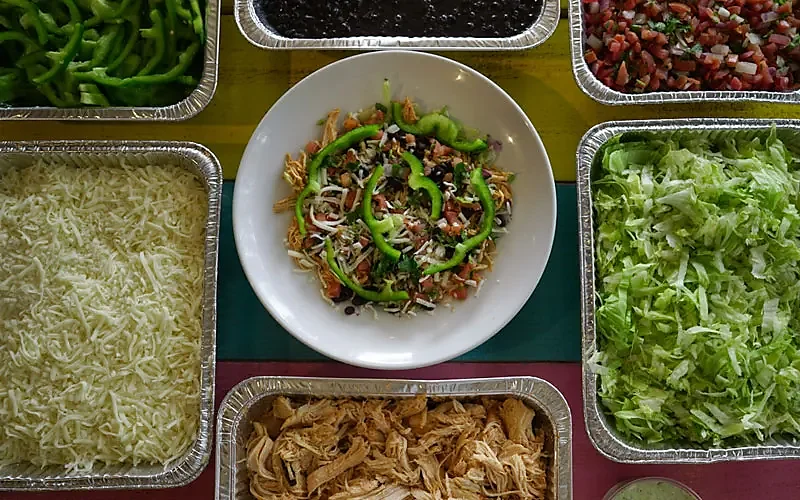 Overhead taco salad bowl surrounded by shredded chicken, cheese and lettuce