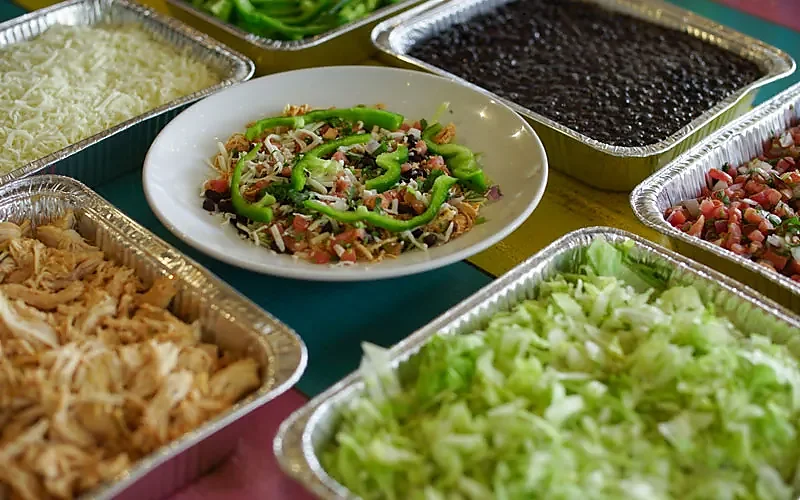 Catering trays of cheese, beans, pico de gallo around taco salad