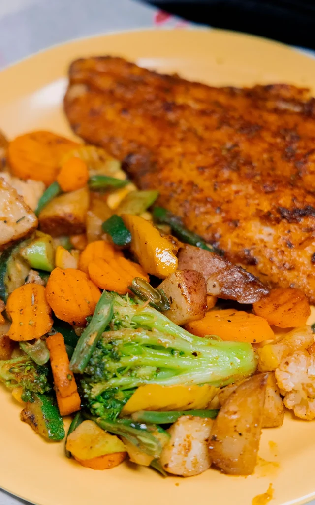 Top-down view: roasted vegetables and crispy fillet on yellow plate.