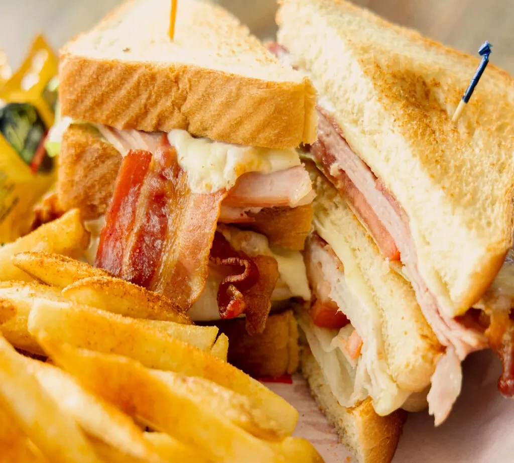 A club sandwich, halved with toothpicks, beside golden french fries.