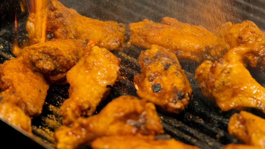Grilled chicken wings with orange glaze and seasoning being sprinkled.