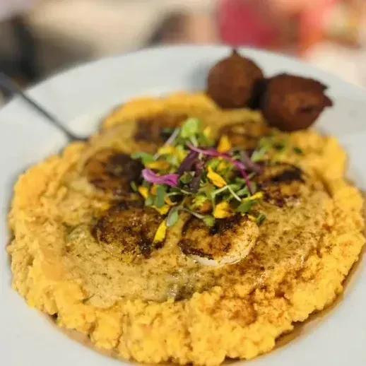 Close-up of shrimp and grits with microgreens, edible flowers, and fritters.