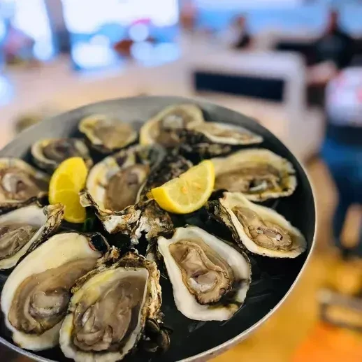 Fresh oysters on the half shell with lemon wedges on a dark tray.