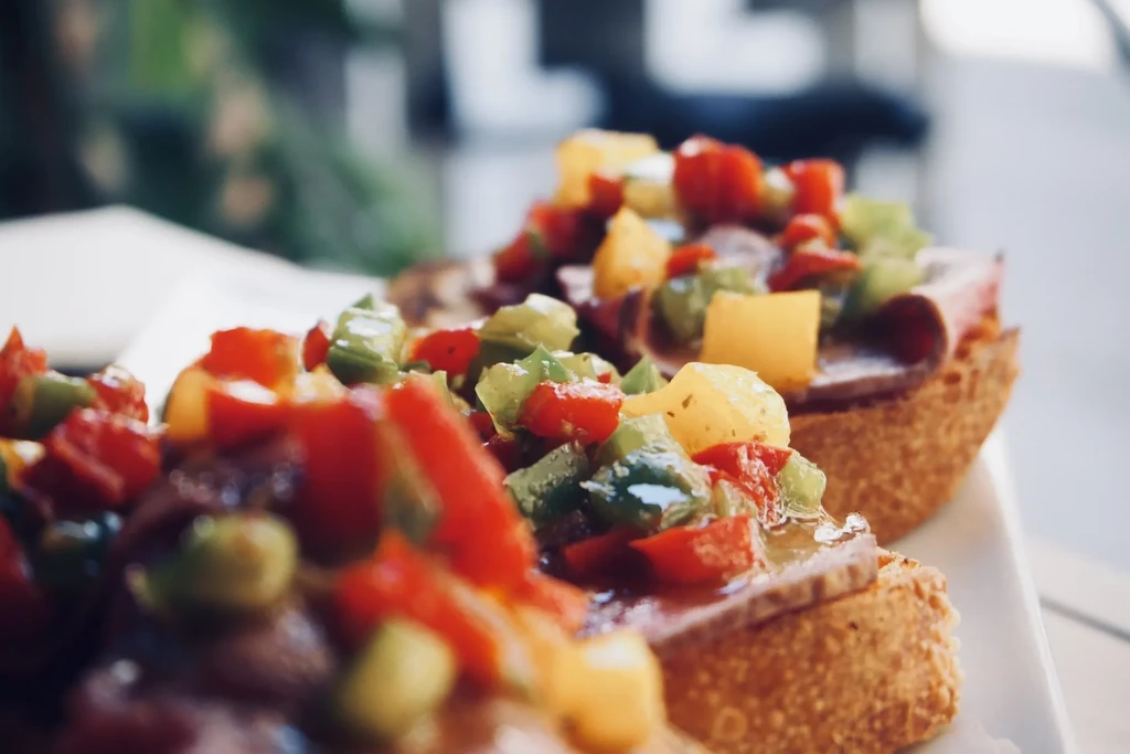 Close-up of open-faced appetizers with colorful diced vegetables and glistening sauce.