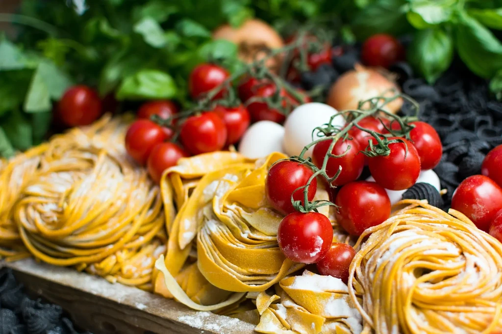 Fresh yellow pasta coils, red tomatoes, green basil, onions, and eggs.
