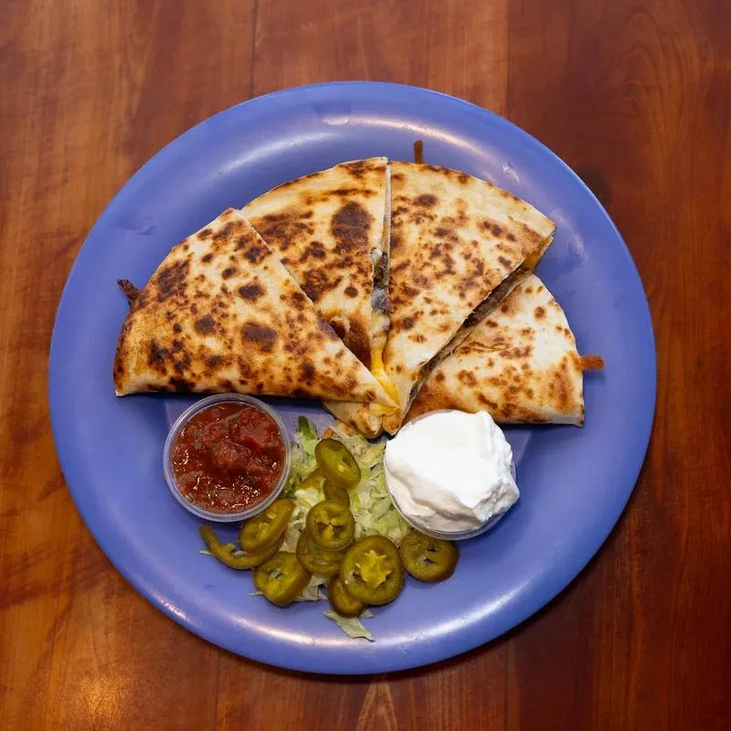 Golden-brown quesadilla, salsa, lettuce, sour cream on a periwinkle plate.