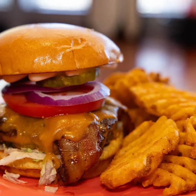Gourmet burger with melted cheese, bacon, lettuce, tomato, and waffle fries.