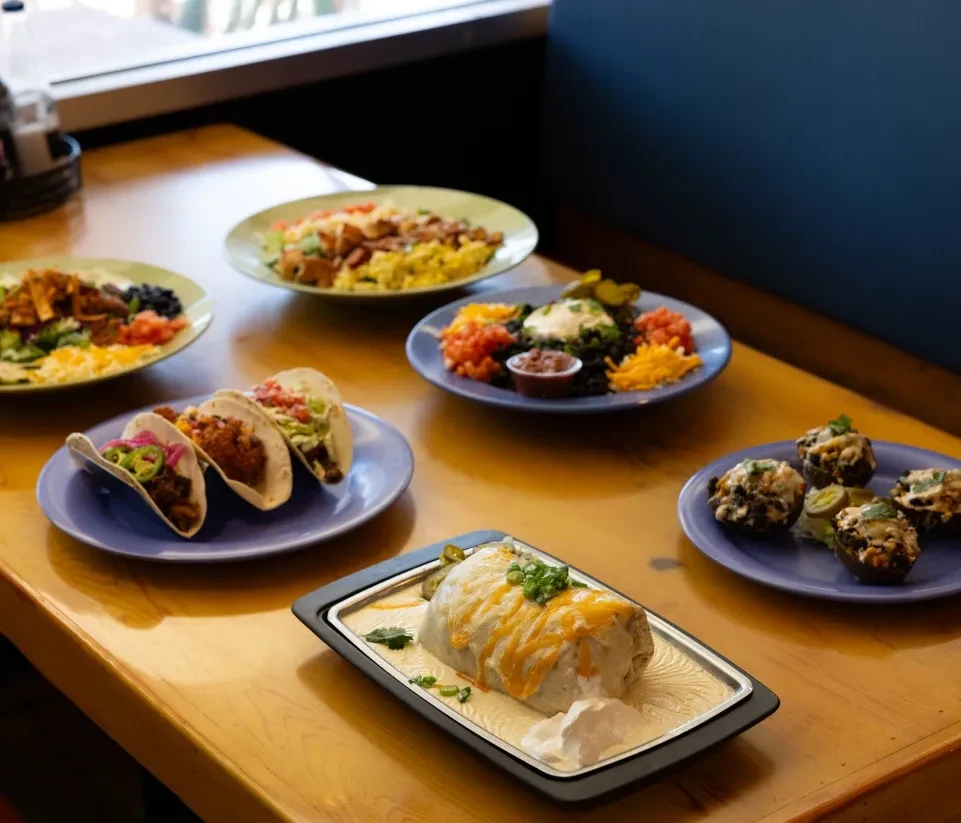 Several plates of Mexican-inspired food arranged on a wooden table.
