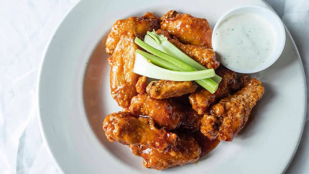 Crispy glazed chicken wings with celery sticks and creamy dip.
