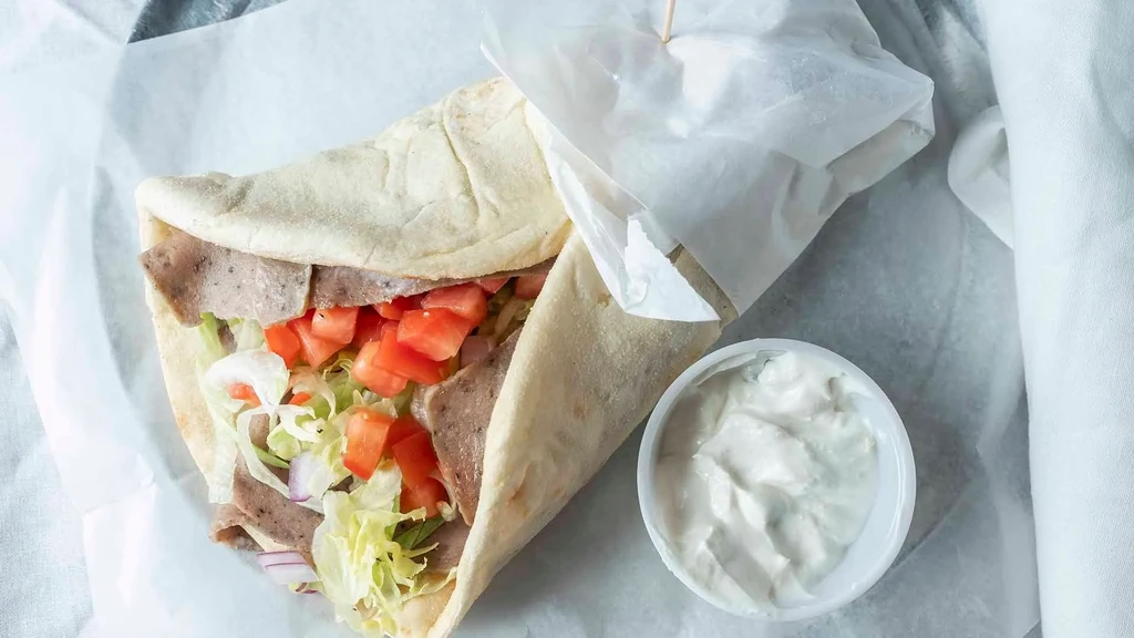 Close-up of a gyro wrap with meat, vegetables, and creamy white sauce.