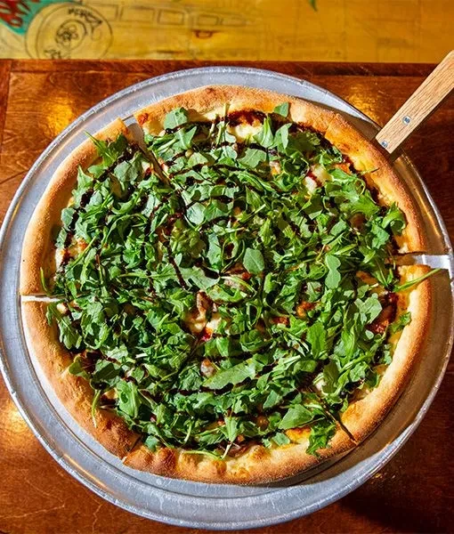 Round pizza with arugula and balsamic glaze on a metallic pan.