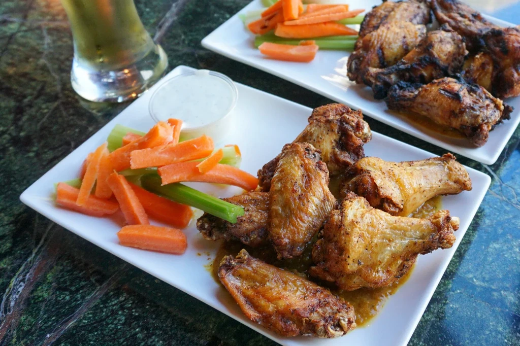 Two plates of crispy chicken wings with vegetables, sauce, and a drink.