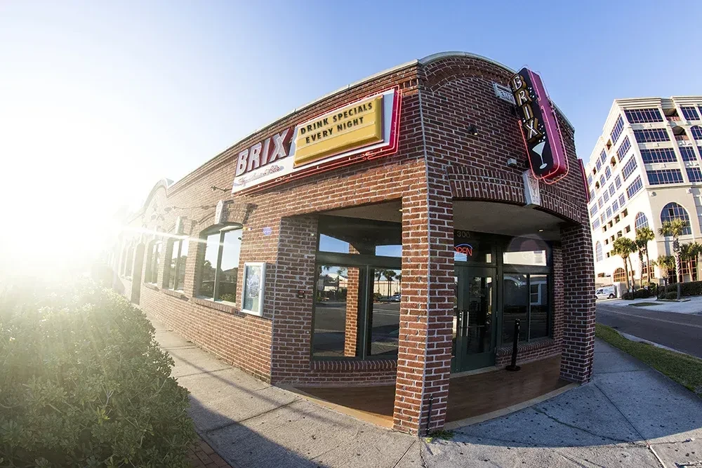 Classic brick building 'BRIX' with neon signs on a sunny urban street.
