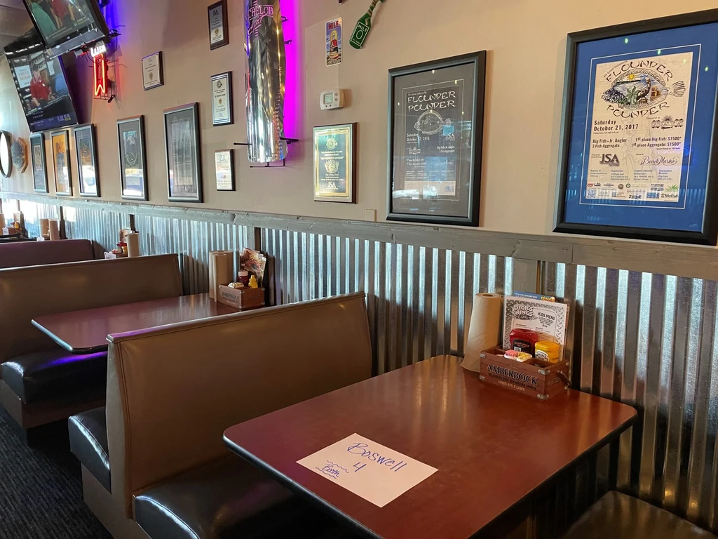 Empty casual restaurant interior with booths, framed awards, and neon lights.