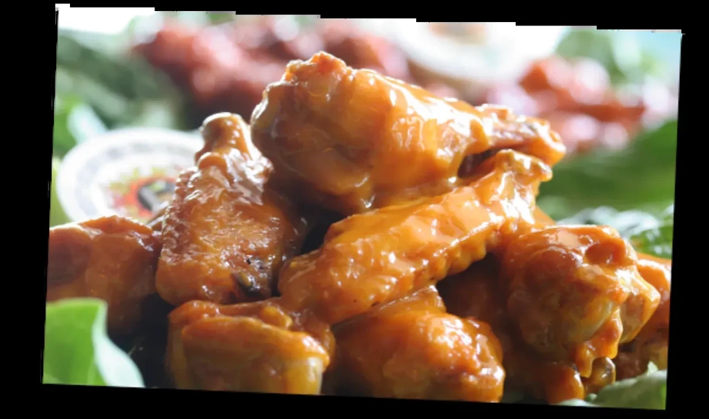 Close-up of chicken wings with glossy orange-brown sauce and green garnish.