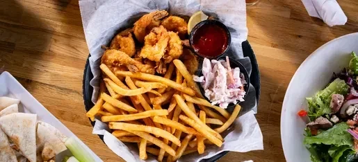 Basket of fried shrimp, french fries, coleslaw, sauces, and salad.