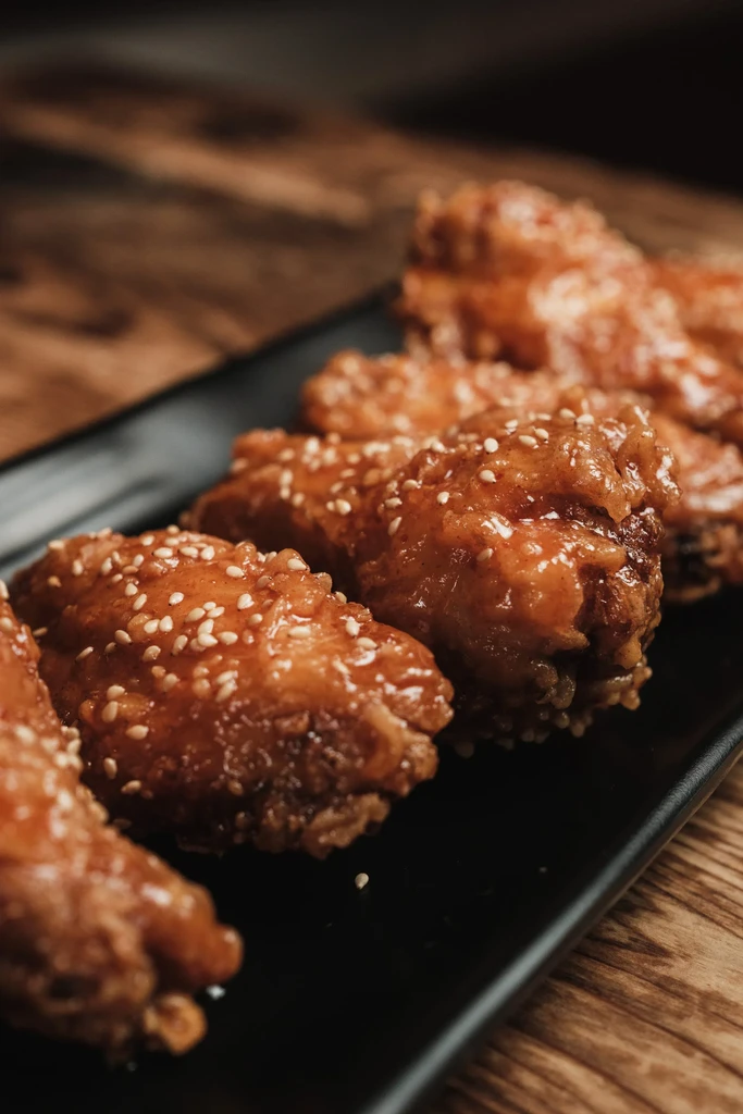 Glossy, sesame-coated chicken wings on a black rectangular plate.
