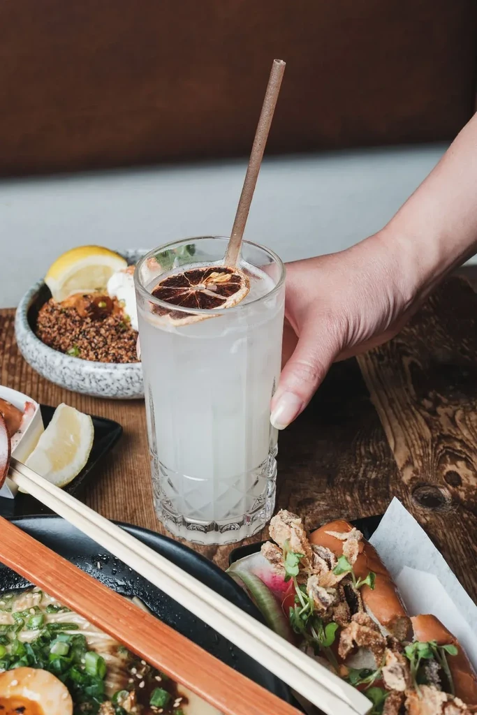 Hand holding a garnished drink, with various modern dishes surrounding it.