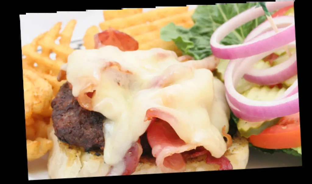 Close-up of a bacon cheeseburger served with waffle fries and a side salad.