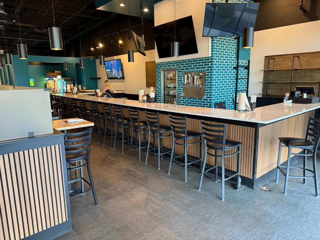 Modern bar interior with L-shaped counter, teal tiled wall, and beer taps.