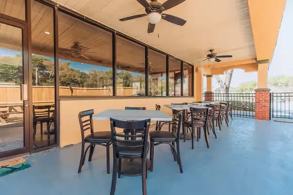 Covered restaurant patio with white tables, dark chairs, and fans.