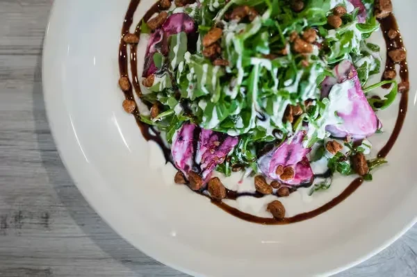 Overhead salad with green leaves, purple ingredients, dressing, and nuts.