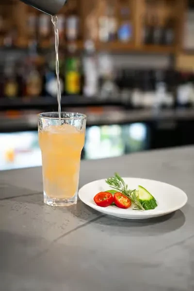 Iced cocktail poured from shaker, garnished with tomato, cucumber, rosemary.