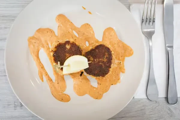 Oval plate with two fried patties, orange sauce, lemon, fork, knife.