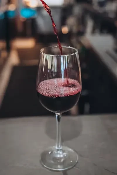 Red wine actively pouring into a stemmed glass, creating foam.