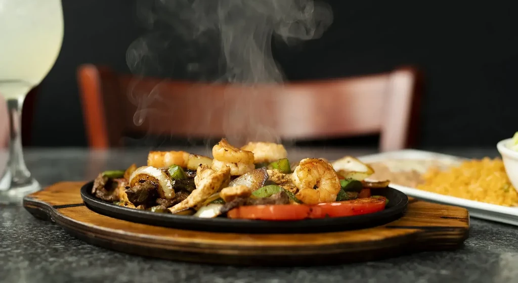 Sizzling cast iron skillet with grilled shrimp, meat, and vegetables.