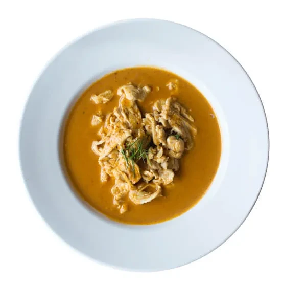 Close-up: Chicken curry in orange sauce, garnished with fresh herbs.