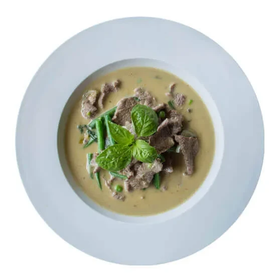 White bowl of green curry, beef, beans, peas, garnished with basil.