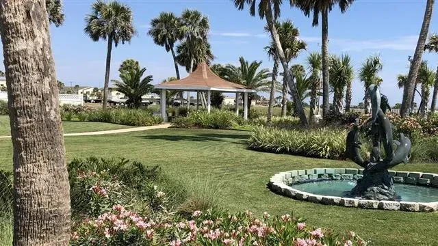 Sunlit garden, green grass, dolphin fountain, white gazebo, palm trees.