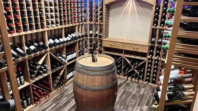 Extensive wine cellar with wooden racks, a barrel, bottle, and glasses.