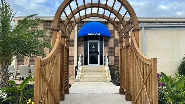 SEAGLASS entrance with blue awning, wooden archway, and patio.