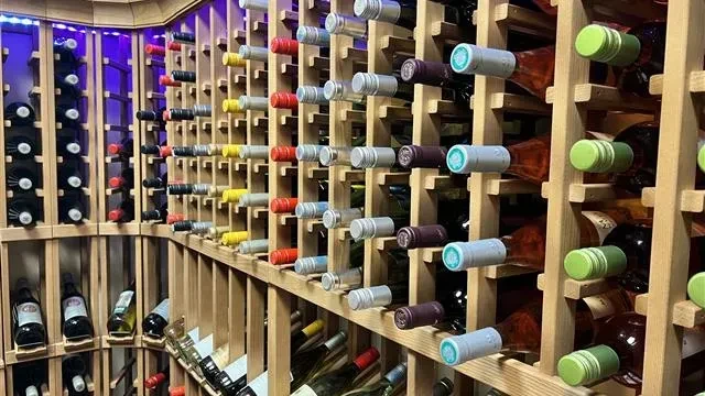 Numerous wine bottles in wooden racks, colorful caps, purple LED lighting.