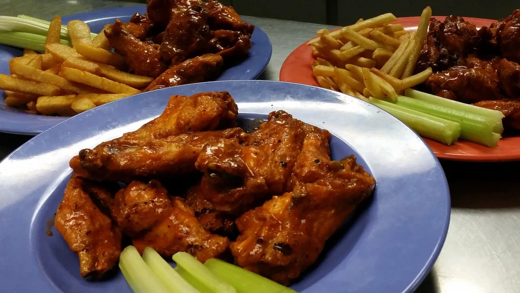 Three plates of sauced chicken wings, fries, and celery sticks.